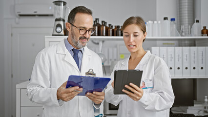 Wall Mural - Two scientists engrossed in reading an intriguing document on clipboard at the lab, speaking about their startling discovery, while working on a touchpad together.