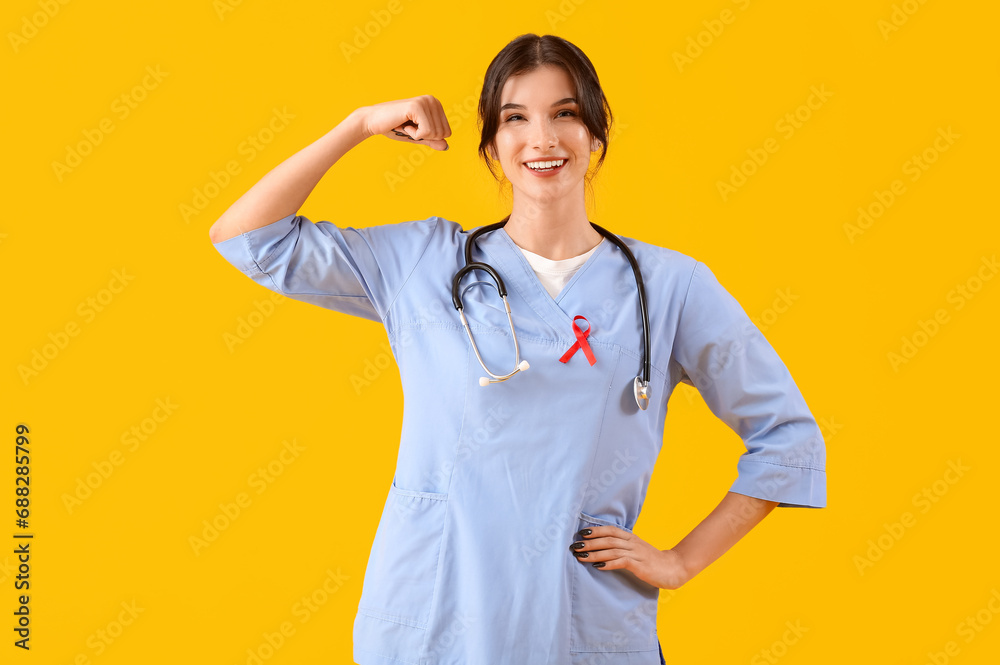 Young female doctor with red ribbon on yellow background. World AIDS day concept