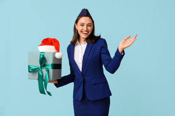 Wall Mural - beautiful stewardess with gift box and santa hat on blue background