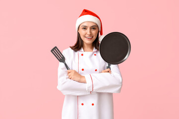 Canvas Print - Beautiful female chef in Santa hat with frying pan and spatula on pink background