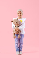 Canvas Print - Little Asian girl after chemotherapy with ribbon and toy bear on pink background. Childhood cancer awareness concept