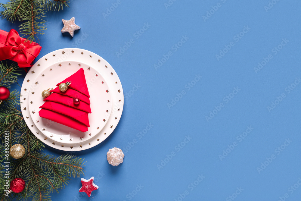 Beautiful table setting with fir branches, Christmas balls, candles and gift box on blue background