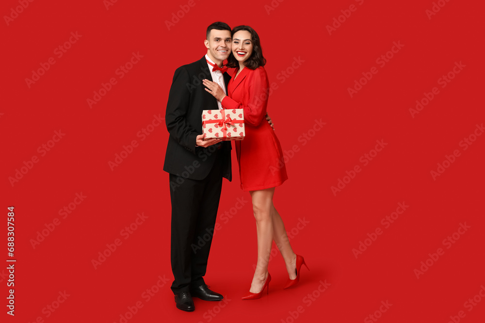 Loving young couple with gift box on red background. Celebration of Saint Valentine's Day