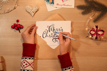 Canvas Print - Female hands writing greeting card on wooden table with Christmas decorations