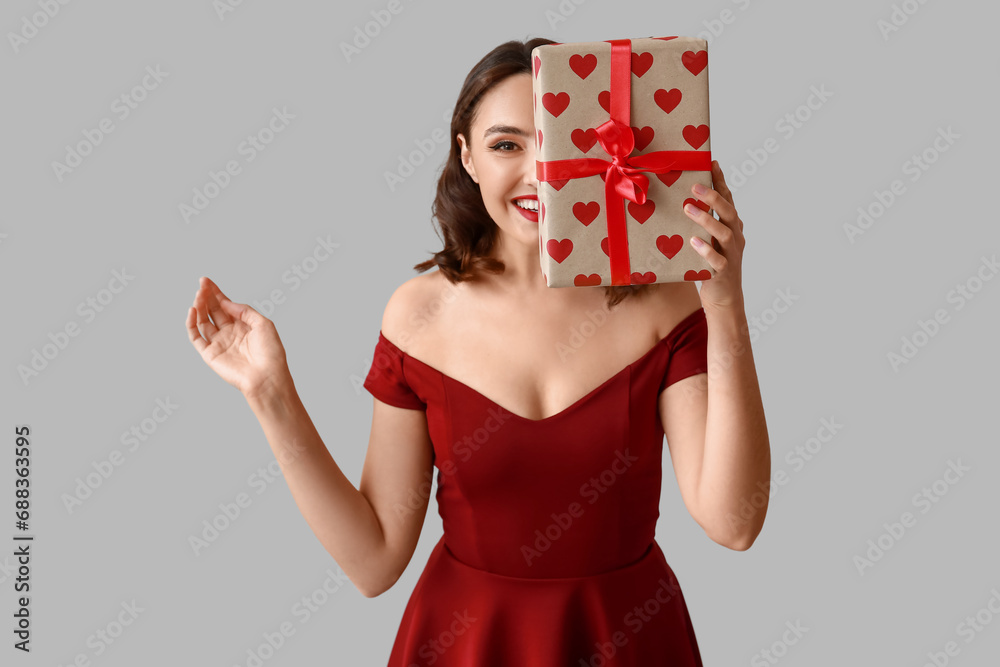 Beautiful young woman with gift box on grey background