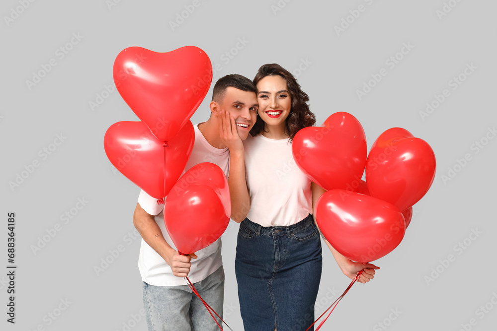 Loving young couple with heart-shaped balloons on grey background. Celebration of Saint Valentine's Day