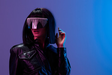 Wall Mural - Shocked awesome brunet woman in leather jacket specular sunglasses open mouth look aside posing isolated in blue violet color light background. Neon party Cyberpunk concept. Copy space. Good offer
