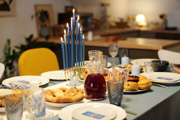  Traditional Hanukkah menorah with nine blue burning candles standing in the center of served table with homemade food and drinks