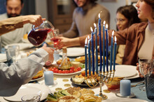 Focus On Blue Burning Candles On Menorah Candlestick Standing On Table Served With Homemade Food And Drinks During Hanukkah Family Dinner