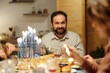 Smiling Jewish man looking at his wife or other family member during Hanukkah dinner while having homemade food and talking