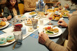 © pressmaster - Hands of young Jewish man sitting by served table with homemade latkes, piece of kugel, dims, fresh cucumbers and tomatoes on his plate