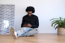 Worker sitting on the floor of his office during a moment of relaxation and break from work writing a text message with his mobile phone
