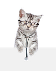 Sticker - Tabby kitten wearing eyeglasses and with stethoscope on his neck looks above empty white banner. isolated on white background