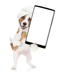 Poster - Funny jack russell terrier puppy with towel on it head holds bath brush and big smartphone with white blank screen in it paw. isolated on white background
