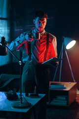 Poster - Young serious businessman with cup of coffee and tablet looking at camera while standing by his workplace in dark office