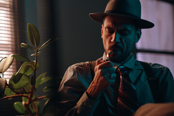 Aufkleber - Young retro man in hat and formalwear lighting cigarette while sitting in front of camera with green domestic plant on his right