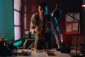 Aufkleber - Young serious businessman or policeman with tobacco pipe in hand bending over workplace with photos and looking at camera