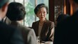 © volga - An elderly Asian woman in an elegant brown suit and pearl necklace conversing at a table.