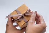 Fototapeta  - Rozpakowywać prezent, pudełeczko ozdobione kokardką trzymane w dłoniach z bliska