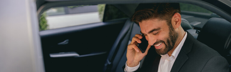 Wall Mural - Handsome businessman in suit using personal computer and making phone call in taxi