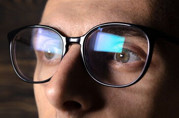 Man works on internet. Reflection at the glasses from laptop..Close up of man's eyes with black female glasses for working at a computer. Eye protection from blue light and rays.