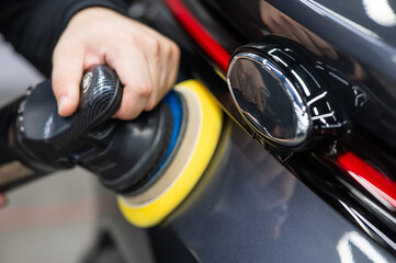 Wall Mural - A mechanic polishes the surface of a car trunk door with a grinding machine.