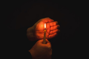 Wall Mural - Burning candle in male hand, religion concept.Black background.