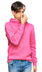 Sticker - Young hispanic man wearing casual pink sweatshirt smelling something stinky and disgusting, intolerable smell, holding breath with fingers on nose. bad smell