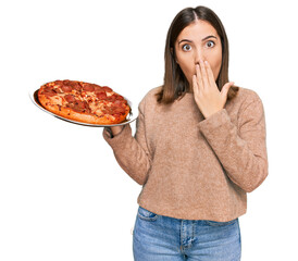 Poster - Young beautiful woman holding italian pizza covering mouth with hand, shocked and afraid for mistake. surprised expression