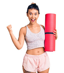 Sticker - Young woman holding yoga mat screaming proud, celebrating victory and success very excited with raised arms