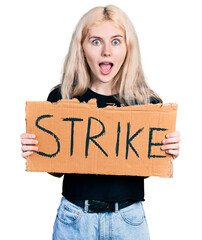 Wall Mural - Young caucasian woman holding strike banner cardboard celebrating crazy and amazed for success with open eyes screaming excited.