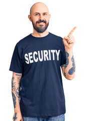 Young handsome man wearing security t shirt cheerful with a smile on face pointing with hand and finger up to the side with happy and natural expression