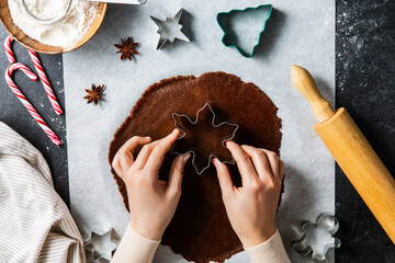 Wall Mural - baking, cooking and christmas concept - close up of hands with mold cutting gingerbread dough on black kitchen table top