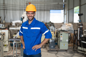 Wall Mural - Portrait of male engineer in uniform smiling and arms akimbo at industrial factory. Technician man standing wearing yellow helmet safety in manufacturing workshop.