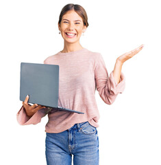 Beautiful caucasian woman with blonde hair working using computer laptop celebrating victory with happy smile and winner expression with raised hands