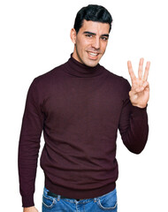 Wall Mural - Handsome hispanic man wearing casual turtleneck sweater showing and pointing up with fingers number three while smiling confident and happy.