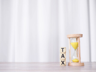 Hourglass and wooden blocks with the word TAX on stack of coins. The concept for manage time to paying tax