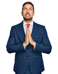 Sticker - Handsome man with beard wearing business suit and tie begging and praying with hands together with hope expression on face very emotional and worried. begging.