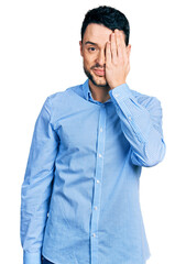 Canvas Print - Hispanic man with beard wearing casual business shirt covering one eye with hand, confident smile on face and surprise emotion.