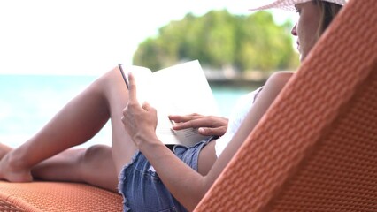 Wall Mural - Woman, relaxing on sunbed and reading book, beach and swimwear for summer vacation. Nature, resting and enjoying holiday, sun tan and seaside in outdoor, beautiful and day off in Indonesia coast