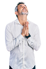 Poster - Middle age hispanic with grey hair wearing casual white shirt begging and praying with hands together with hope expression on face very emotional and worried. begging.