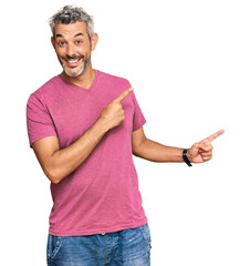 Canvas Print - Middle age grey-haired man wearing casual clothes smiling and looking at the camera pointing with two hands and fingers to the side.