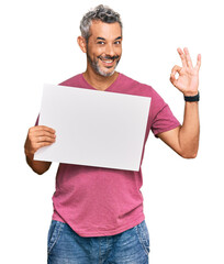 Sticker - Middle age grey-haired man holding blank empty banner doing ok sign with fingers, smiling friendly gesturing excellent symbol