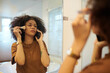 © DragonImages - Hispanic woman talking on phone with friend and applying makeup