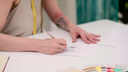 Wall Mural - Lady designer draws clothes model on paper at table in fashion atelier tailor makes pencil sketch of apparel for women in sewing studio closeup dressmaking industry