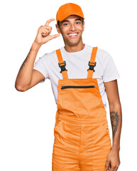 Sticker - Young handsome african american man wearing handyman uniform smiling and confident gesturing with hand doing small size sign with fingers looking and the camera. measure concept.