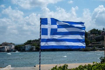 Wall Mural - Greek flag on flagpole waving in the wind in front of blur island background. Greece sign symbol.