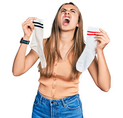 Sticker - Hispanic young woman holding socks angry and mad screaming frustrated and furious, shouting with anger looking up.