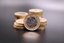 New One Pound Coins On A Dark Background.  Piles Of Coins And One Standing In Front.  British Coin.  British Pound. Dark Background.  Black Background