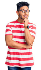 Wall Mural - Handsome latin american young man wearing casual clothes and glasses looking confident at the camera smiling with crossed arms and hand raised on chin. thinking positive.